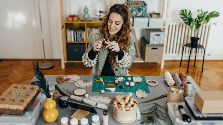 A smiling Caucasian woman is working on a project with wooden beads