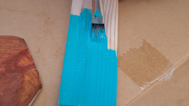 A small paintbrush is covering a board with turquoise paint