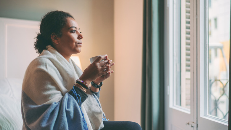 Woman wrapped in blanket standing next to an uninsulated window