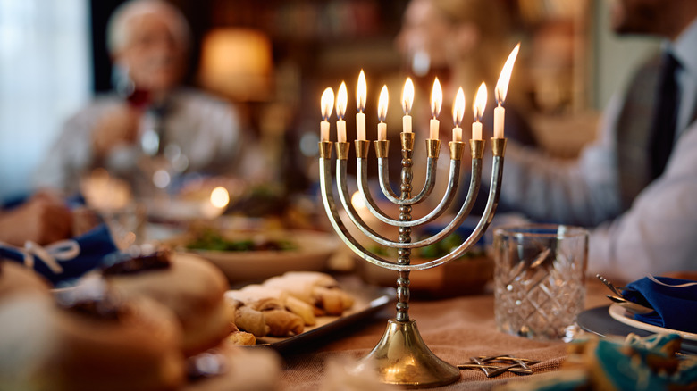 A fully lit Hanukkah menorah on a dining room table surrounded by family and food