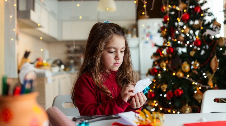 A girl creating a craft in front of a Christmas tree.