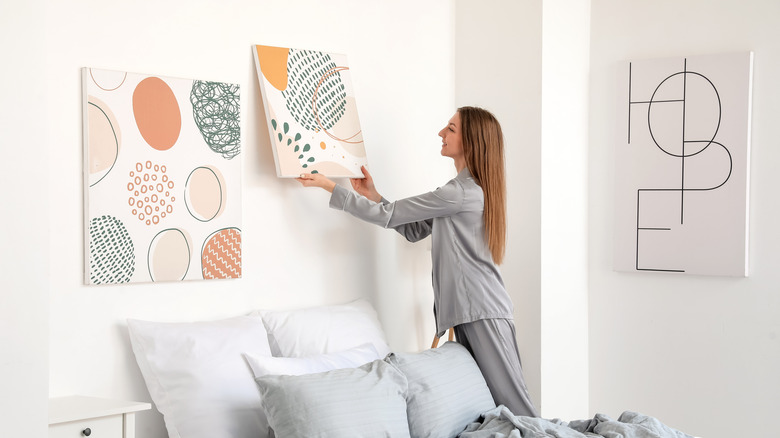 Woman hanging wall art on bedroom wall