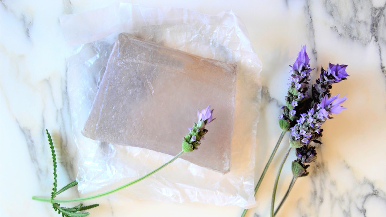 Bar of clear soap on marble table with purple flowers