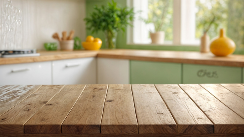 A wooden island is in the foreground with a bright green and white kitchen in the background with yellow decor accents.