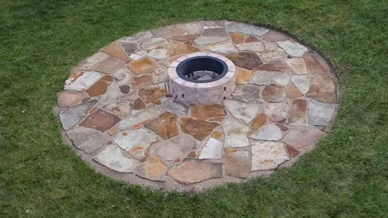 A finished flagstone patio fire pit lays in the grass