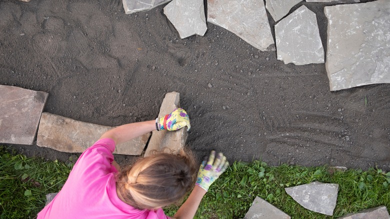 A person lays flagstones in a yard