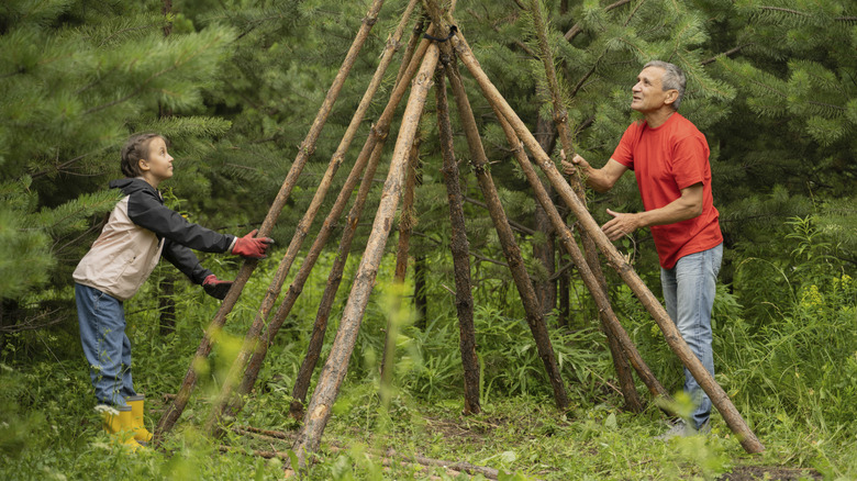 A man and young girl building a teepee using logs