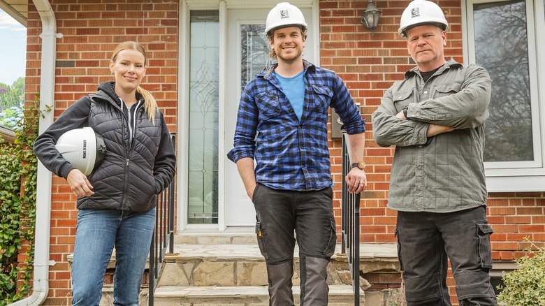 Sherry Holmes, Mike Holmes Jr, and Mike Holmes in front of a brick home.