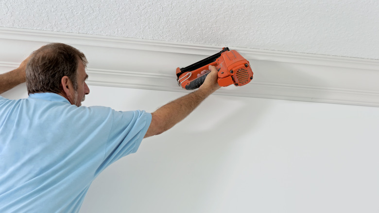 A man hangs crown molding along a popcorn ceiling