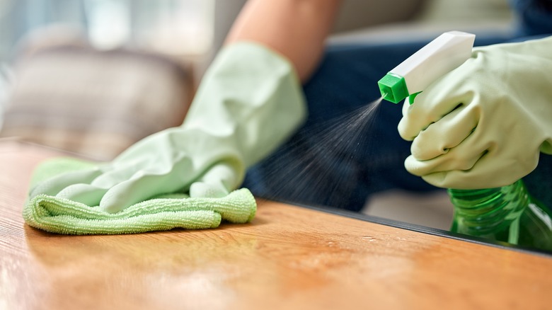 Gloved hands with a spray bottle and green microfiber cloth