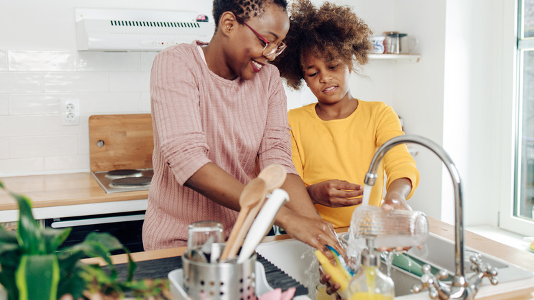 Black woman, child washing dishes