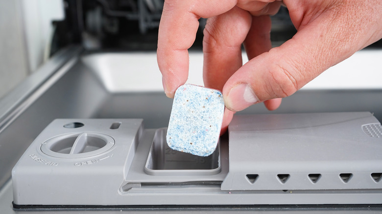 person adding detergent to dishwasher