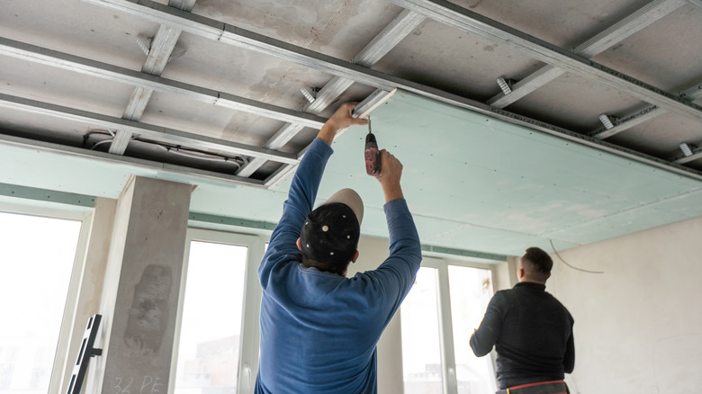 Two men installing ceiling tiles on dropped ceiling