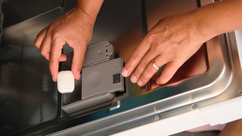 person putting dishwasher cleaner tablet in dispenser