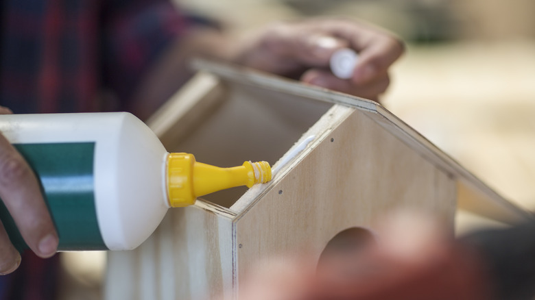 A person uses wood glue to attach the roof of a bird house