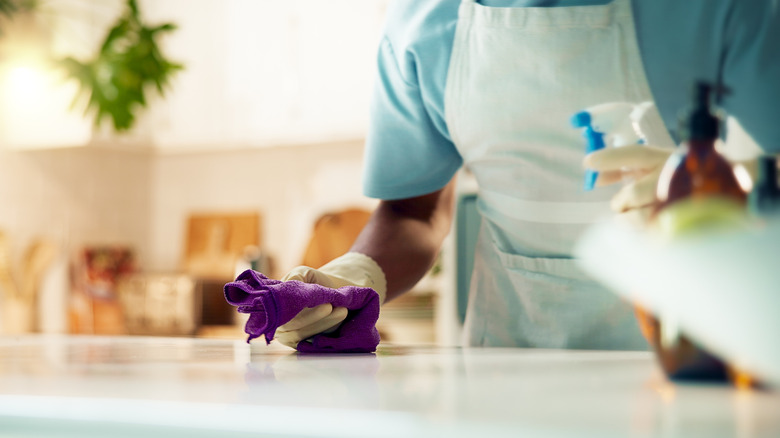 A person in an apron with a spray bottle and a cloth wiping down a countertop