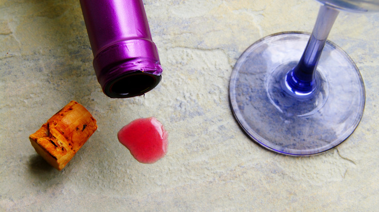 Wine spilled on a stone countertop, surrounded by a bottle, cork, and glass