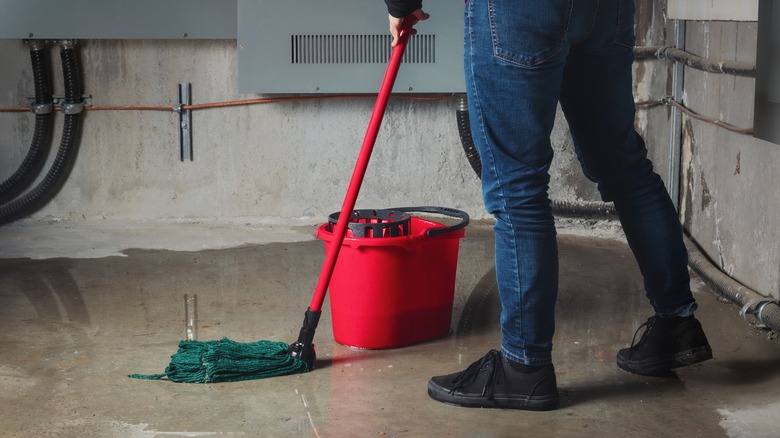 Person mopping up water from burst pipes in basement