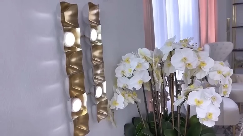 A DIY light fixture made from bowls and wooden dowels is shown hanging above a white floral plant.