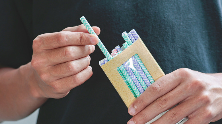 A person pulls a colorful drinking straw out of a packet.