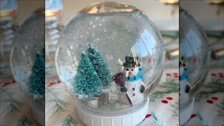 A snow globe made with a snowman figurine and tiny pine trees with glitter swirling in the water.