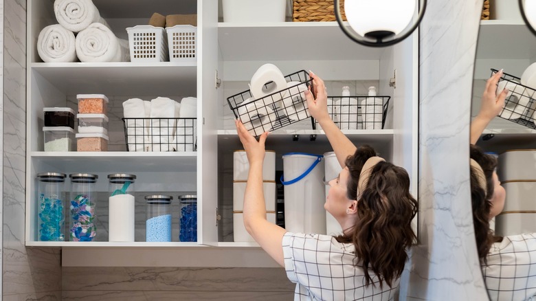 woman putting basket of toilet paper on shelf