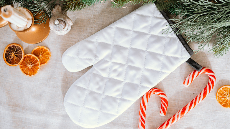 White oven mitt with greenery, candy canes, and dried orange slices.