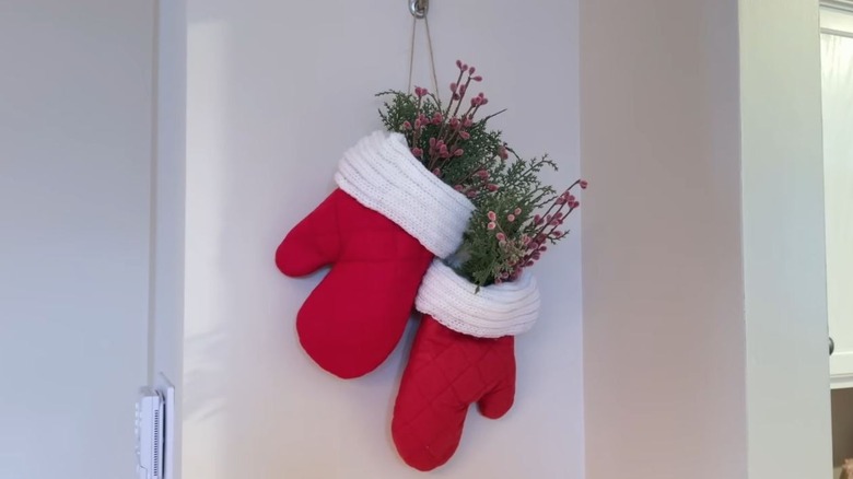 Two red winter mittens hang on the wall with winter flowers stuffed inside.