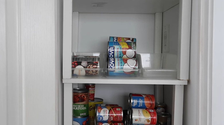 White kitchen cabinet shelves holding canned goods in soda can holder