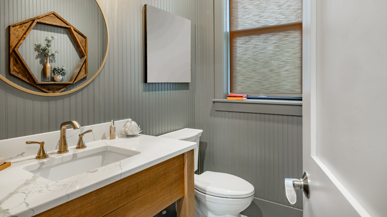 A milky gray color-drenched powder room decorated with marble vanity and brass faucet.