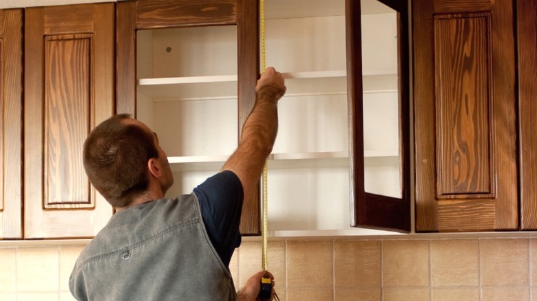 Man measuring the height of wood wall-mounted cabinet doors