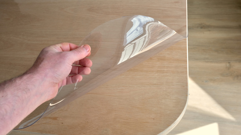 Hand lifting the corner of a clear vinyl tablecloth