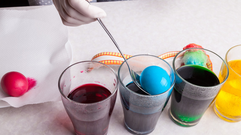 Hand wearing a latex glove dips an egg in a glass of blue dye