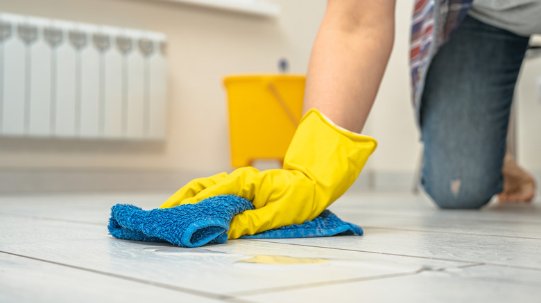 Woman cleaning porcelain floor tiles with microfiber cloth wearing rubber gloves