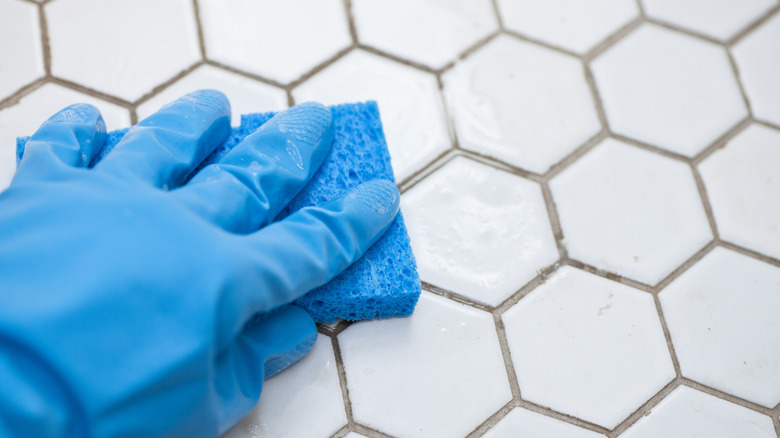 Person cleaning white porcelain tiles with a sponge wearing rubber gloves