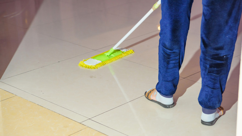 Person in sweatpants using a yellow mop to clean porcelain tiles