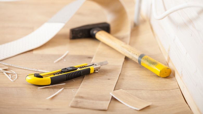 A mallet and a box cutter laying on a sheet of wood patterned linoleum