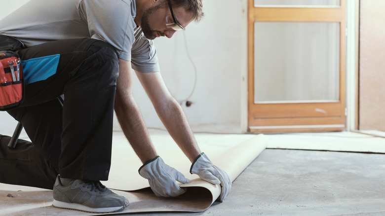 Man laying down layer of linoleum flooring