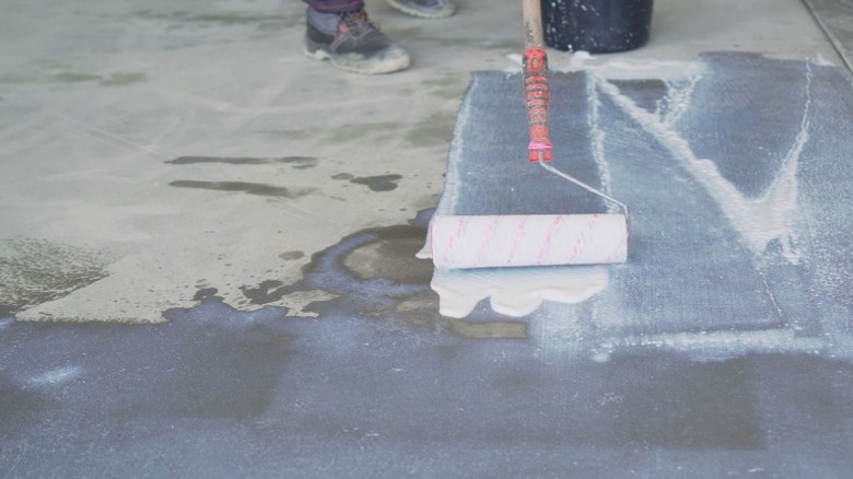 person using long handled roller to apply opaque sealant to concrete subfloor