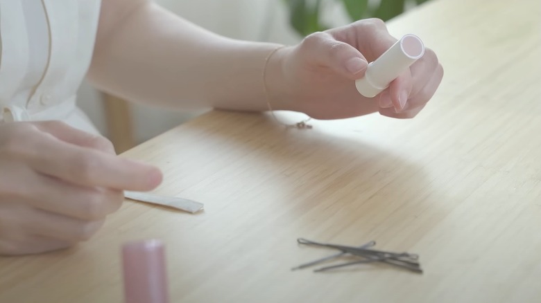 Woman holding empty lipstick tube preparing to place bobby pins inside