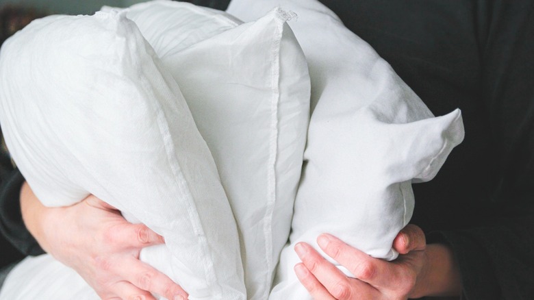 Person in black shirt carrying three white bed pillows