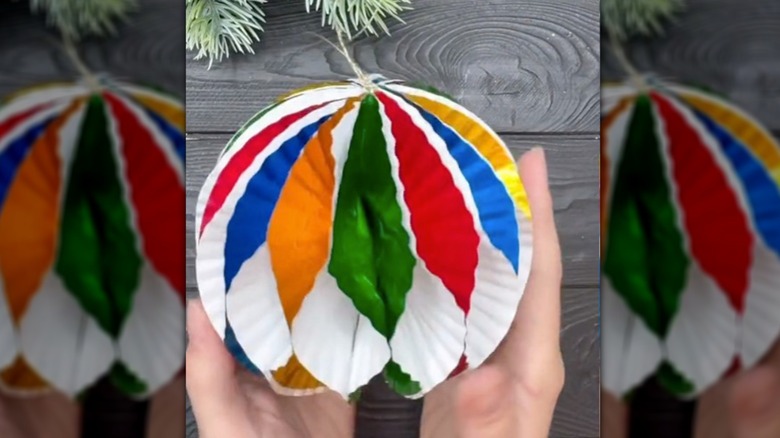 Woman's hand holds a multi-colored paper ornament made of cupcake liners