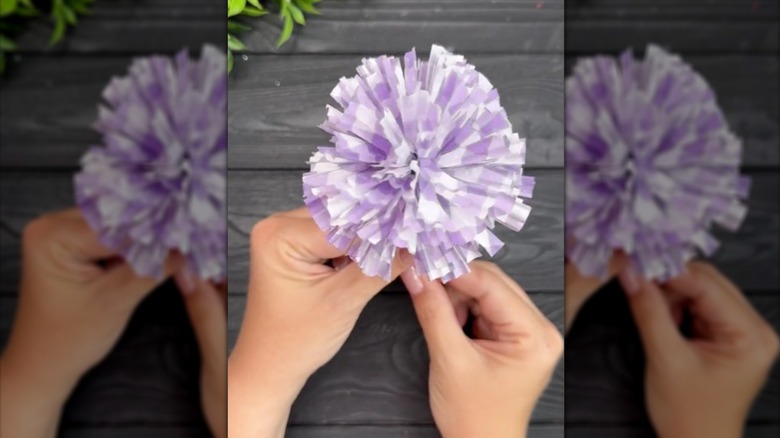 Woman's hand holds a purple and white paper flower made from cupcake liners