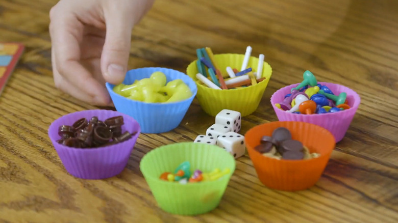 Man hand over a group of cupcake liners, each filled with pieces from a board game