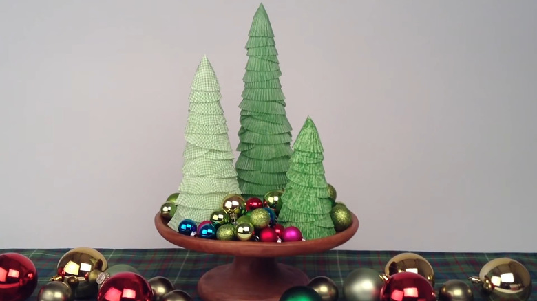 Cupcake liner trees in varying shades of green in a bowl decorated with shiny ornaments