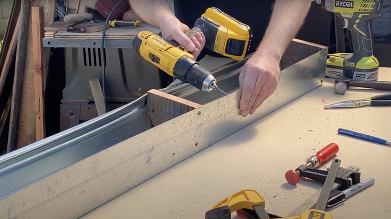 A person drills into a metal gutter that they're converting into a window box garden.