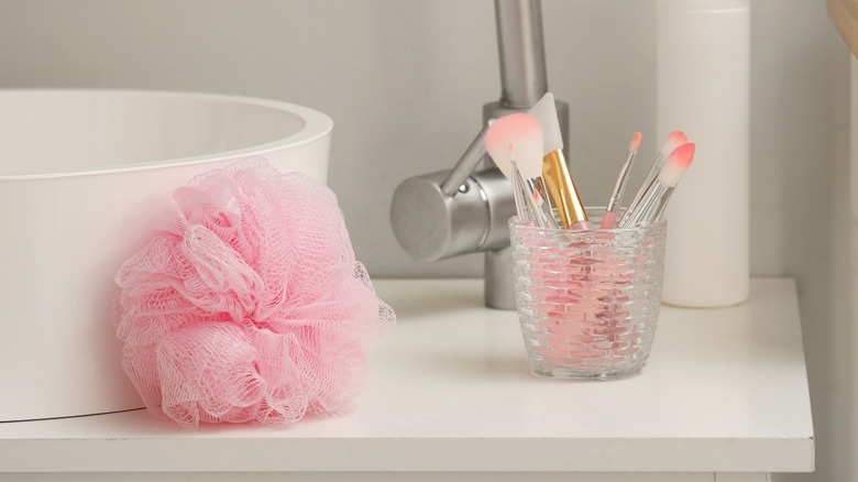 Makeup brushes in a holder and pink loofah near the sink in a bathroom