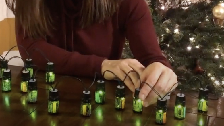 Woman installing holiday lights in essential oil bottles.