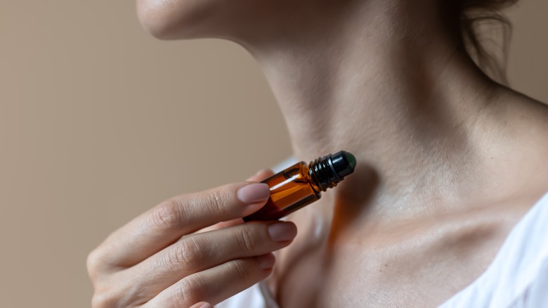 Woman applying scent roller from small amber bottle.