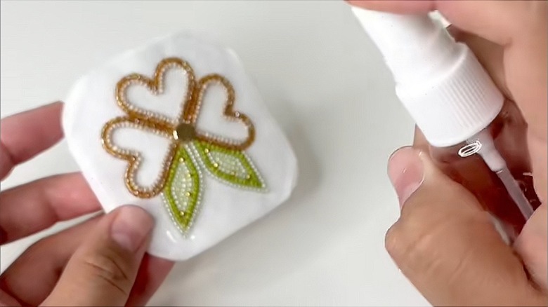 Close-up of a hand spraying beadwork on paper